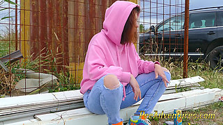 Hipster girl with a hoodie pee trough her jeans and pee next to the wheel of the car